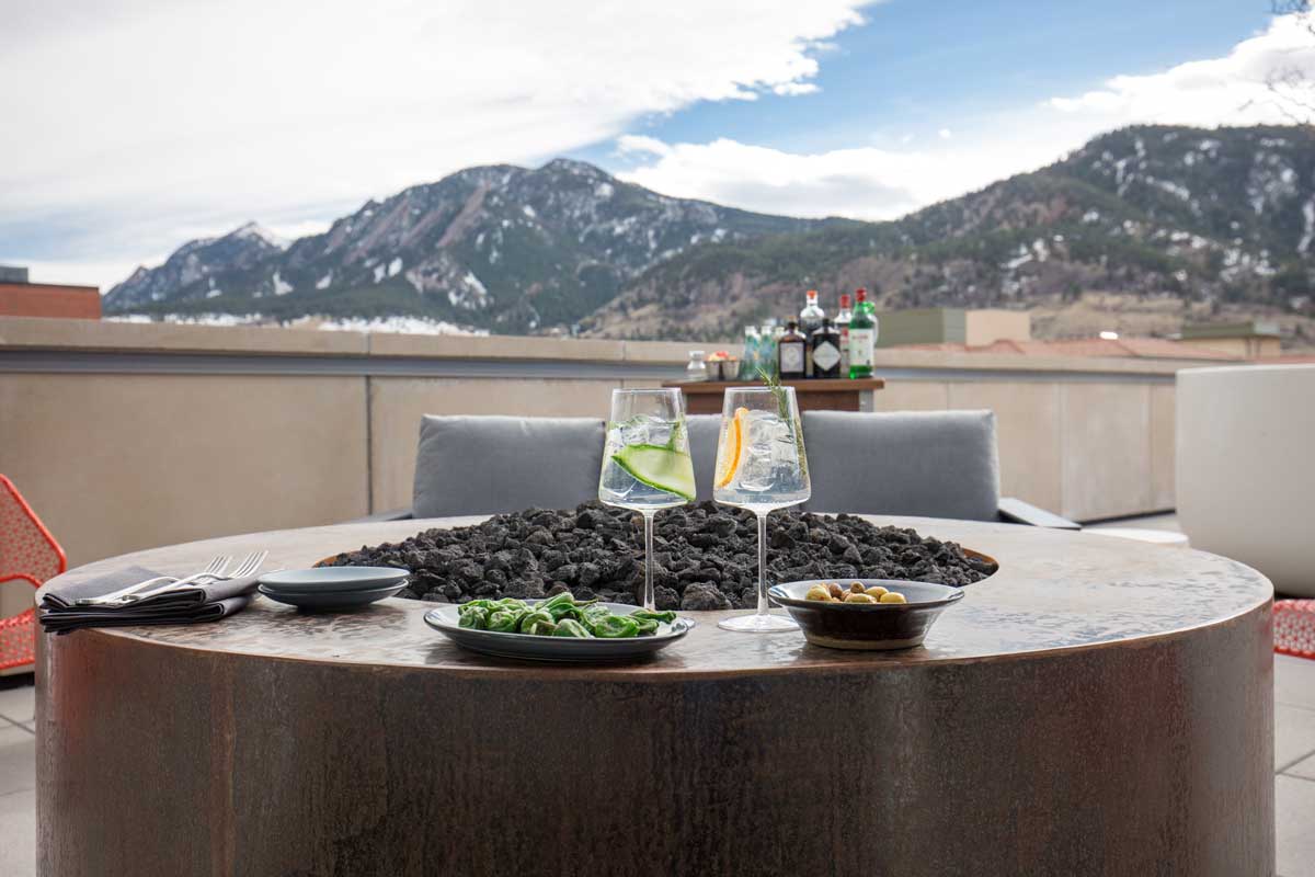 Two stemmed water-glasses, one with lemon and the other with cucumber, sit on a round table with a firepit in the middle at a rooftop in Corrida.