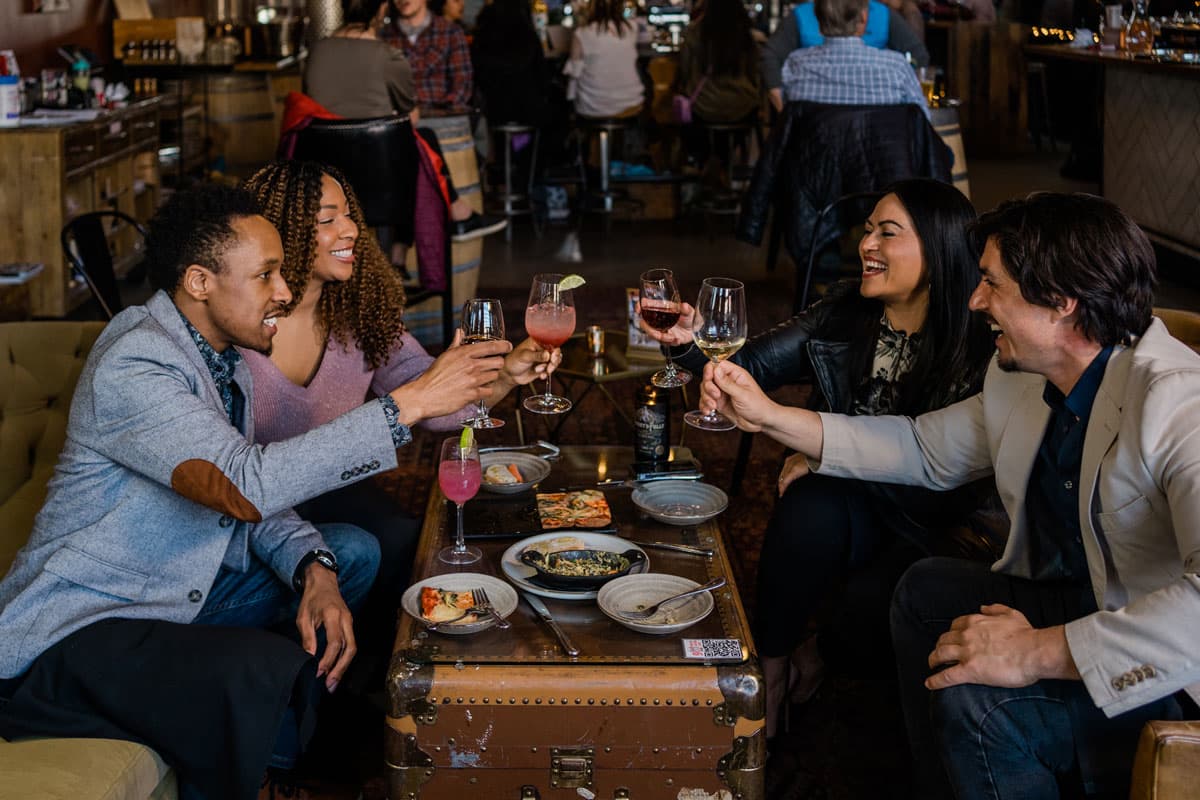 Two well-dressed couples sit around a table and clinks glasses at a 1920s-inspired tasting room in Denver, Colorado.