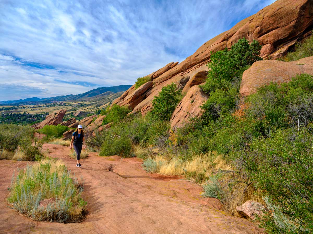 A hiker walks along a trail surrounded by a red-rock landscape