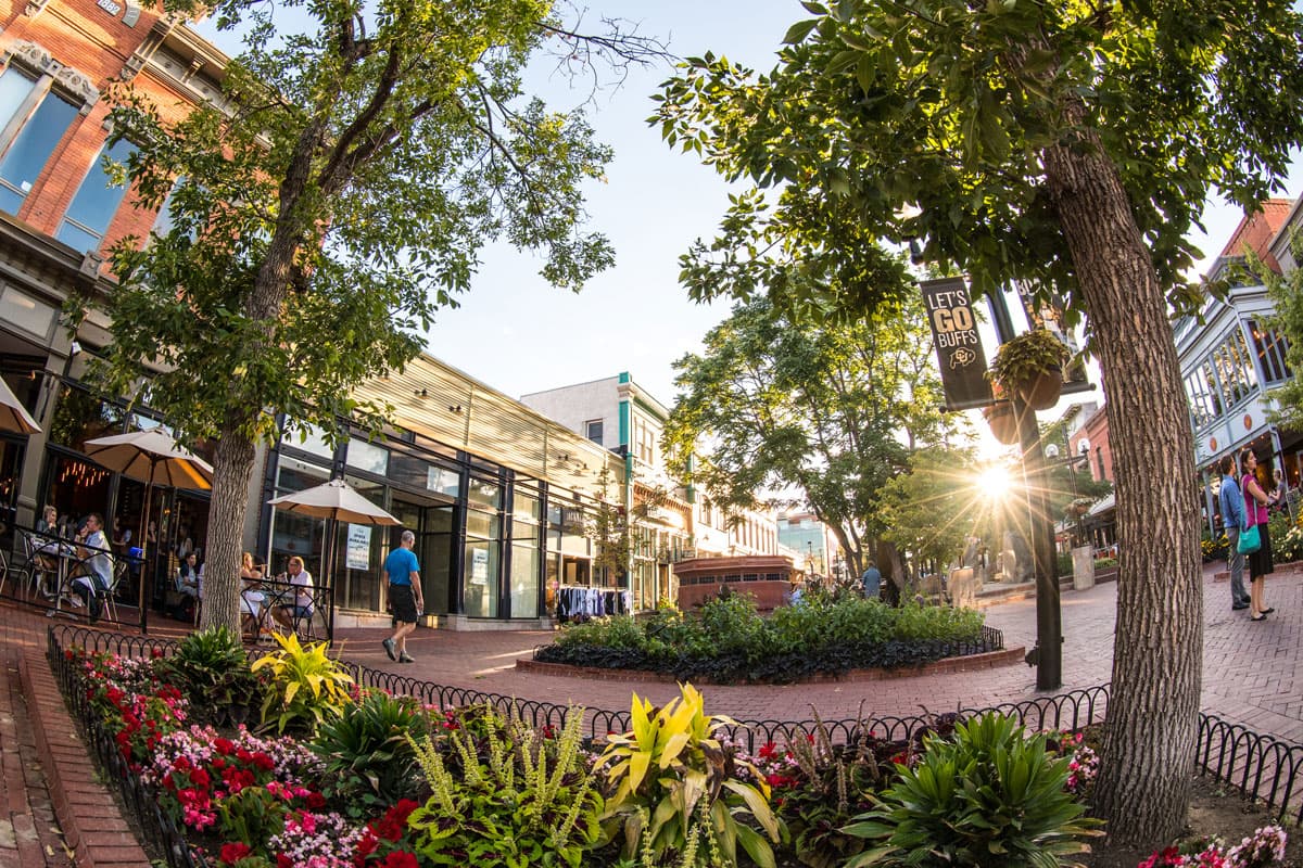 In summer, downtown Boulder's Pearl Street is filled with trees covered in green leaves, excited shoppers and vibrant flowers in garden beds.
