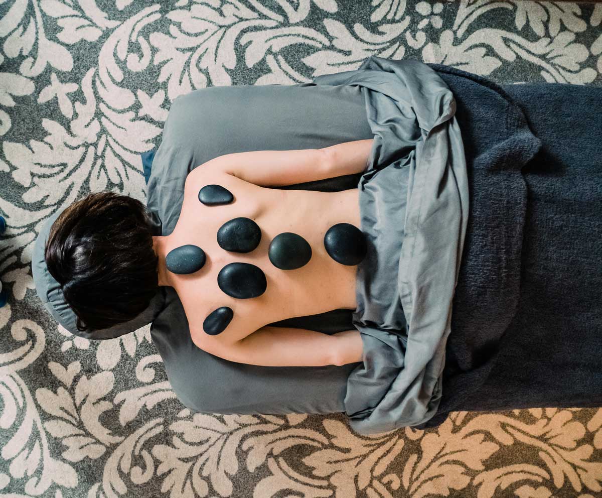 A woman lays facedown on a massage table and has hot stones on her back