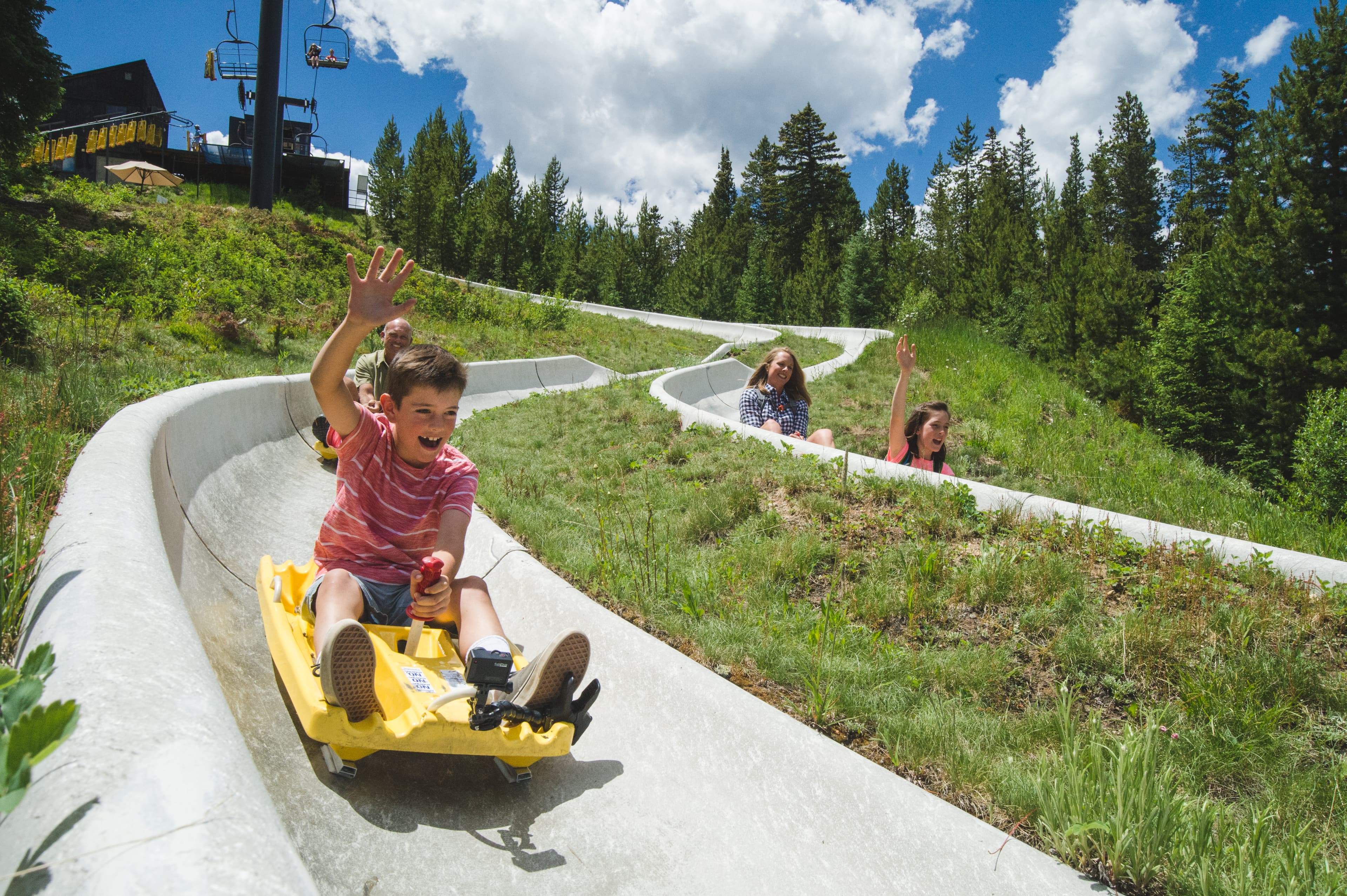 Kids smile and laugh as they slide down the Winter Park Alpie Slide during the summer time.