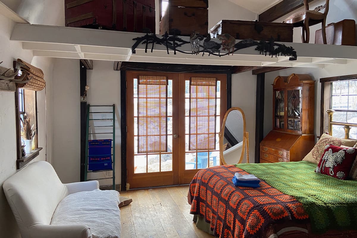 A guest room at Cedar Ridge Ranch in Colorado features a bed, sofa and antique furniture on display on a shelf in the rafters.