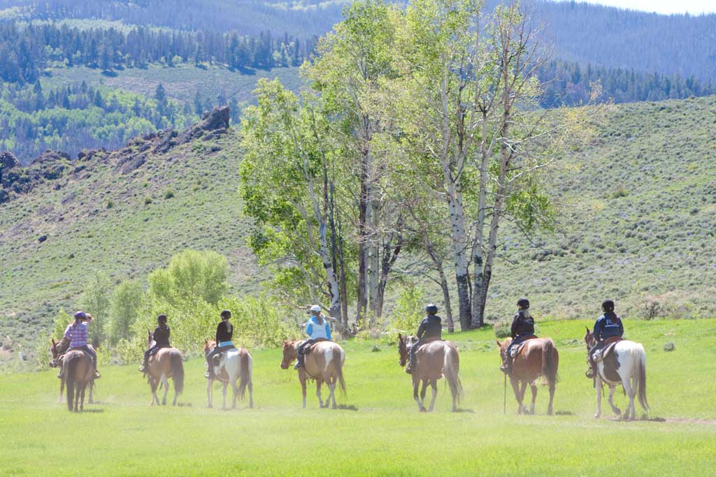 Guests horseback ride on green pastures at C Lazy U Ranch in Granby, Colorado