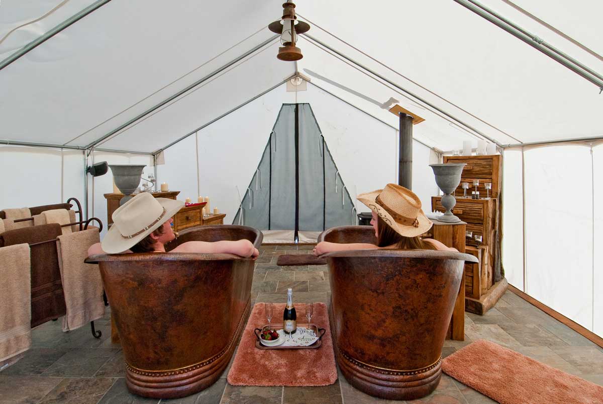 C Lazy U Ranch guests soak in his and hers tubs with Champagne flutes between them in a tent