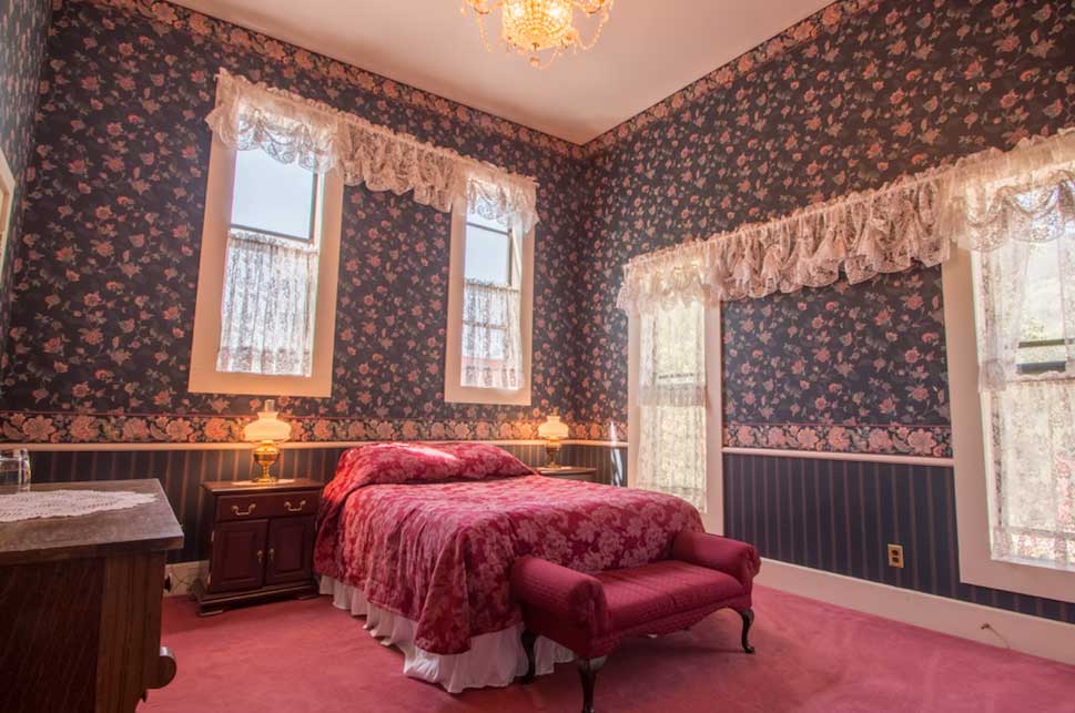 A Victorian-styled room at Rico Mine Shaft Inn, complete with decorative wallpaper and crimson bedcovers