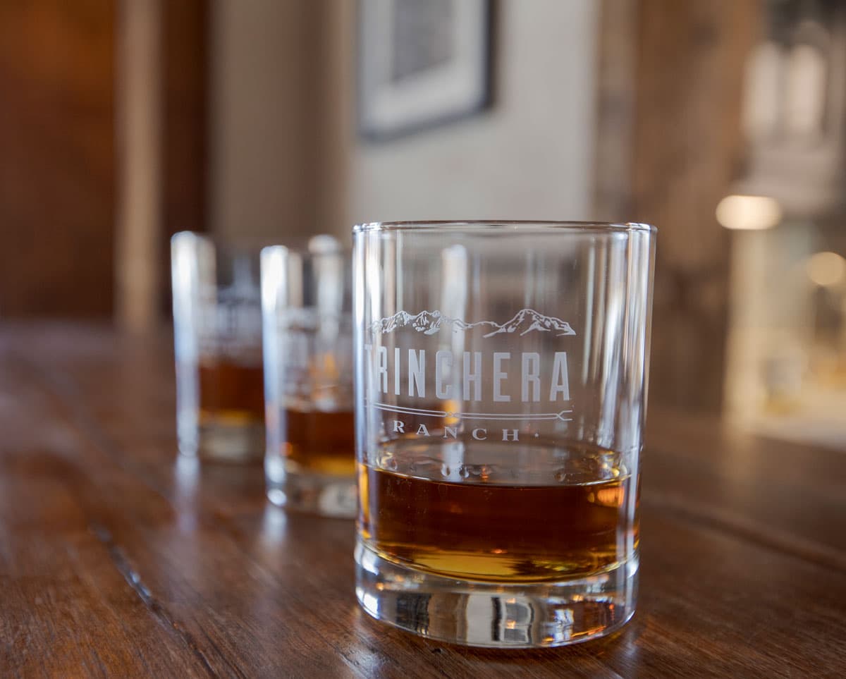 Whiskey in fancy Trinchera Blanca Ranch glasses sitting on a wooden bar