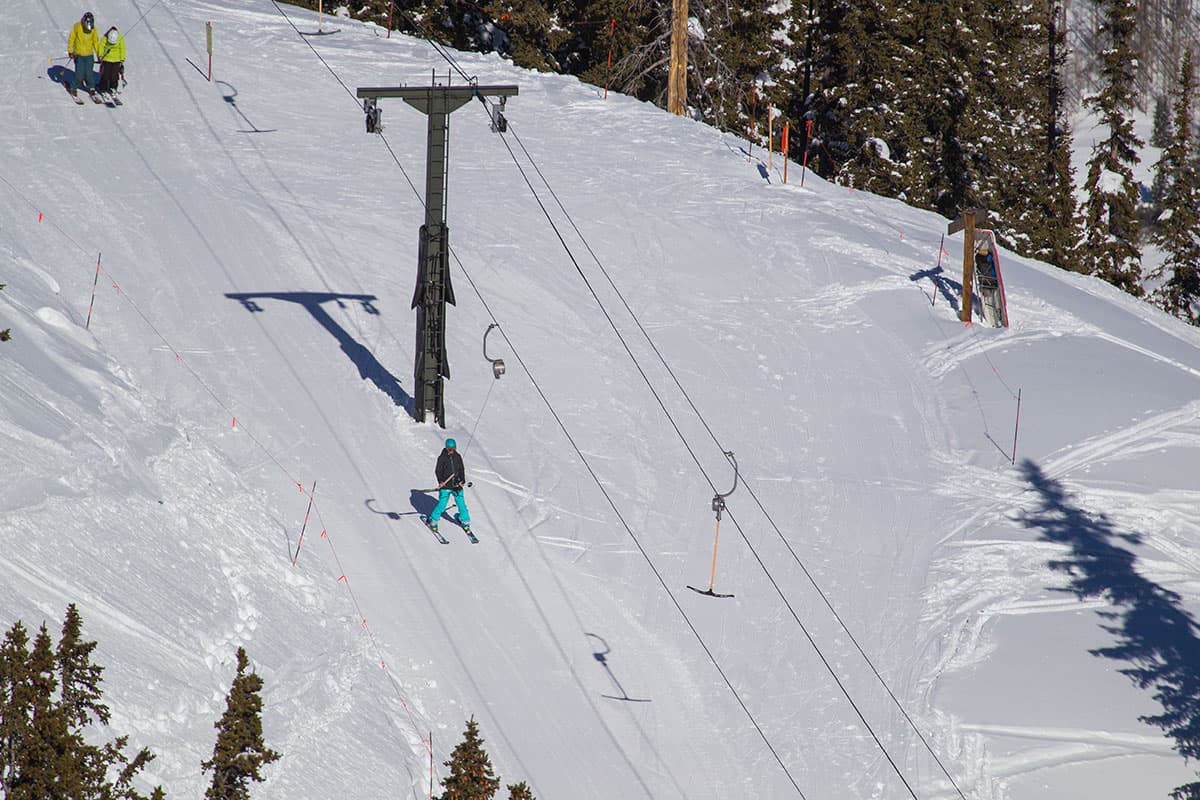 Aerial view of skiers using a T-bar ski lift on a steep, snowy mountain