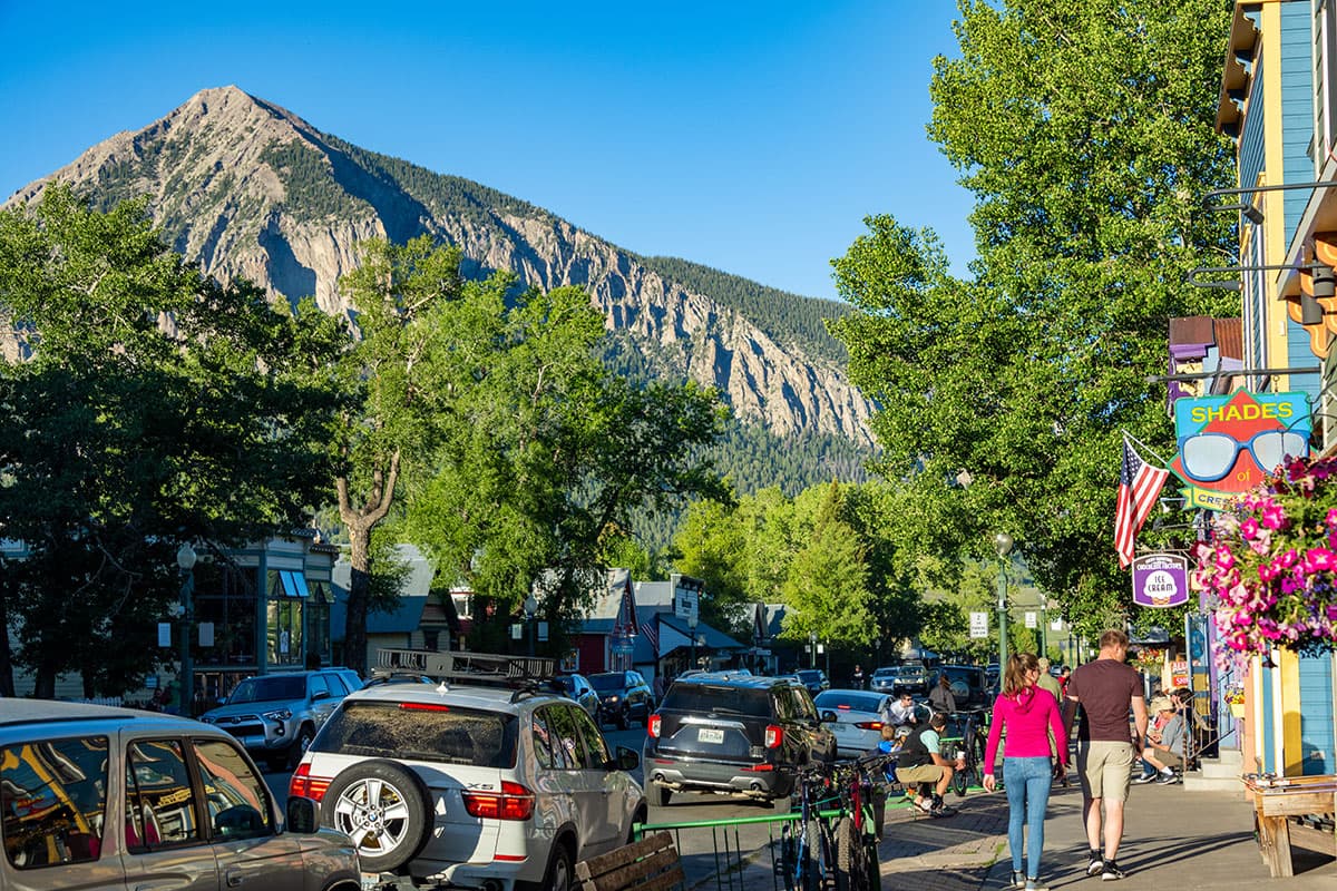 Street scene of people walking down a sidewalk among restaurants and shops, with a mountain looming in the background.