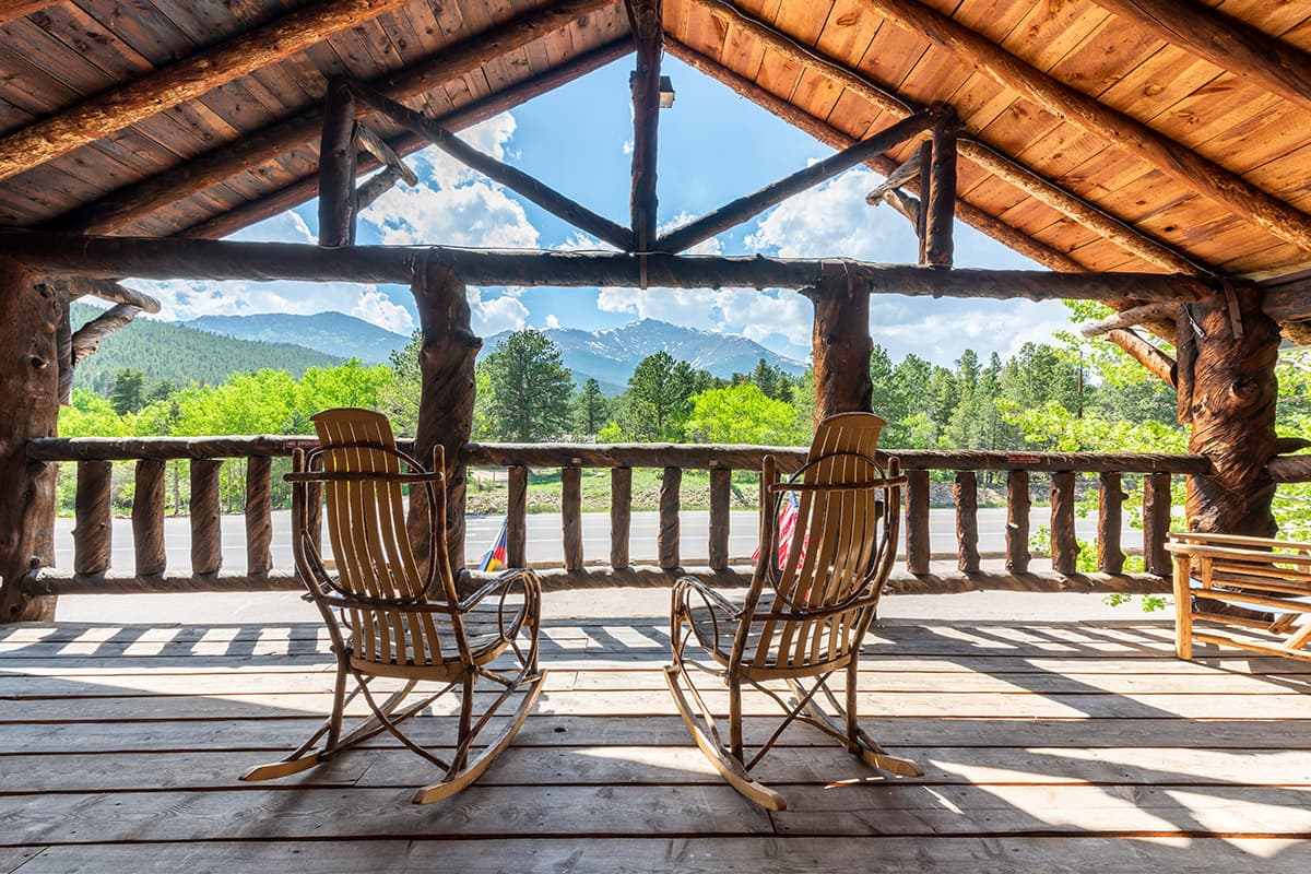 Two rocking chairs sit on a roofed balcony at Meeker Park Lodge with a unobstructed view of towering Rocky Mountain peaks.