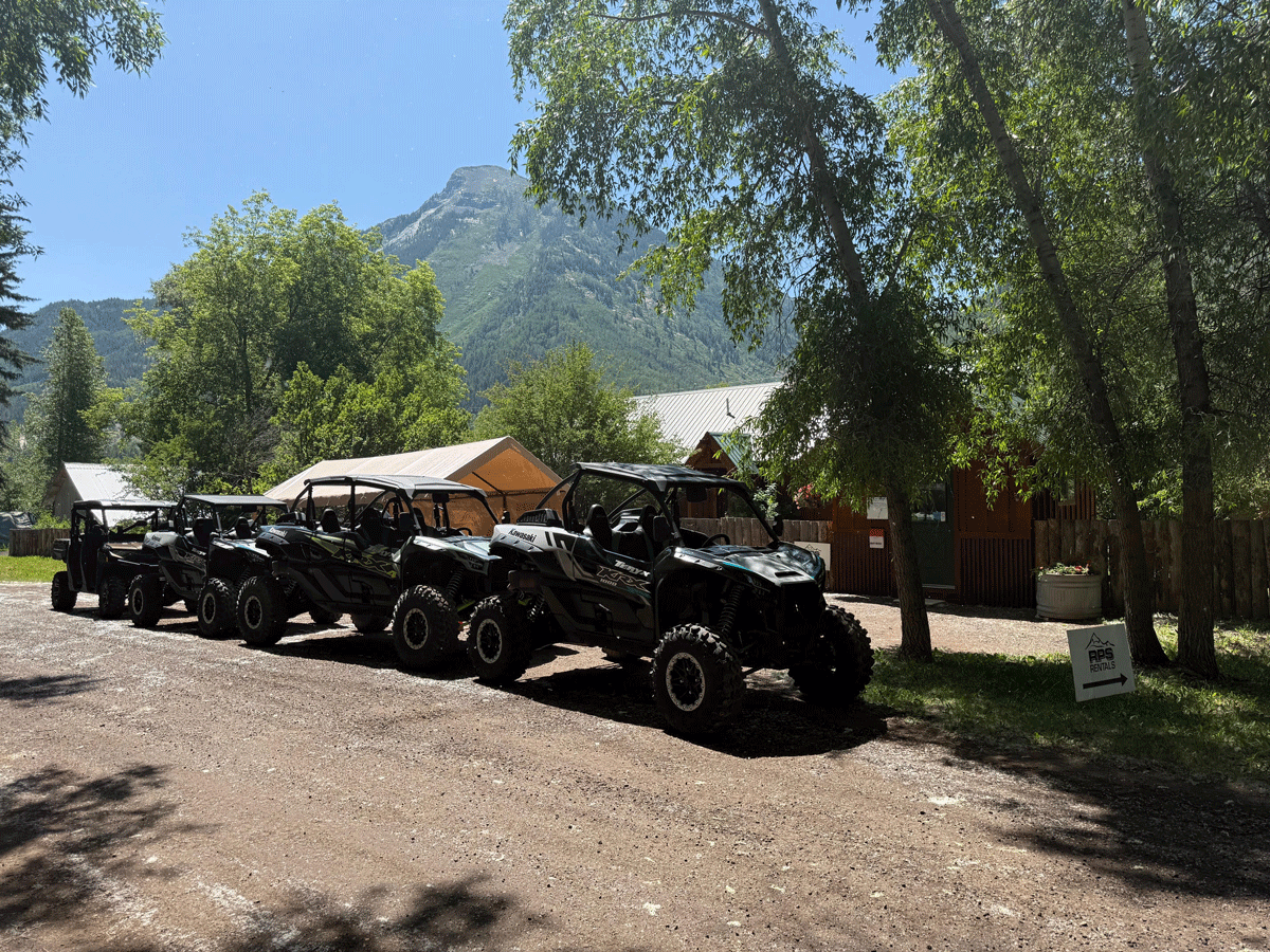 RPS rental vehicles lined up on a dirt road next to tall trees and a mountain in the background in Marble, Colorado.