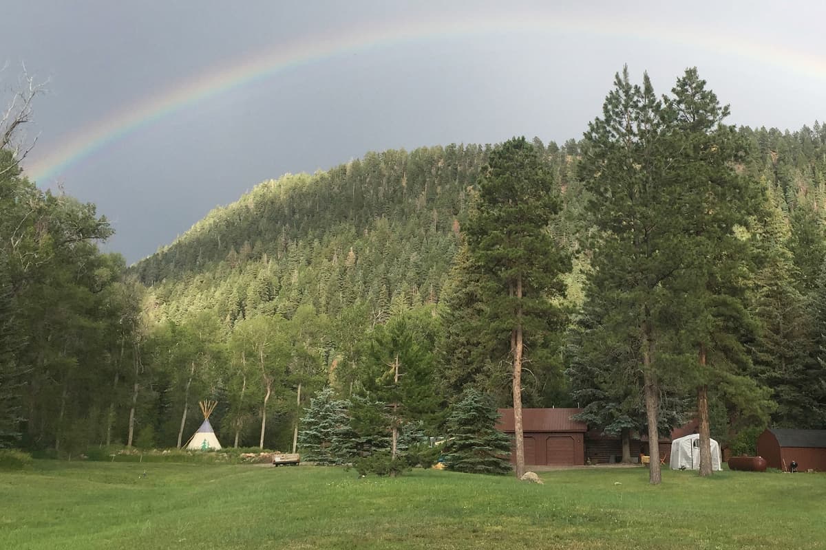 A rainbow arcs over the pine forest and open meadow surrounding O-Bar-O Cabins near Durango, CO.