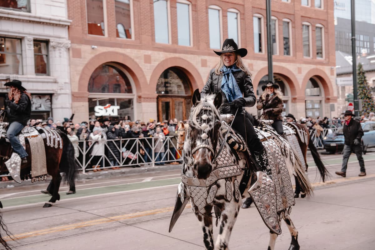 A woman on a horse rides down a street in Dnever as part of the National Western Stock Show Parade