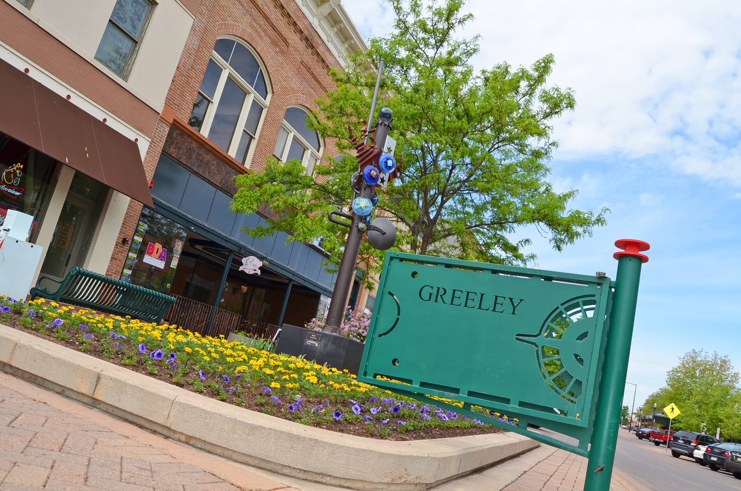 A green metal sign that says "Greeley" welcomes visitors to the downtown shopping area, which is decorated with flower beds, colorful lightposts and benches.