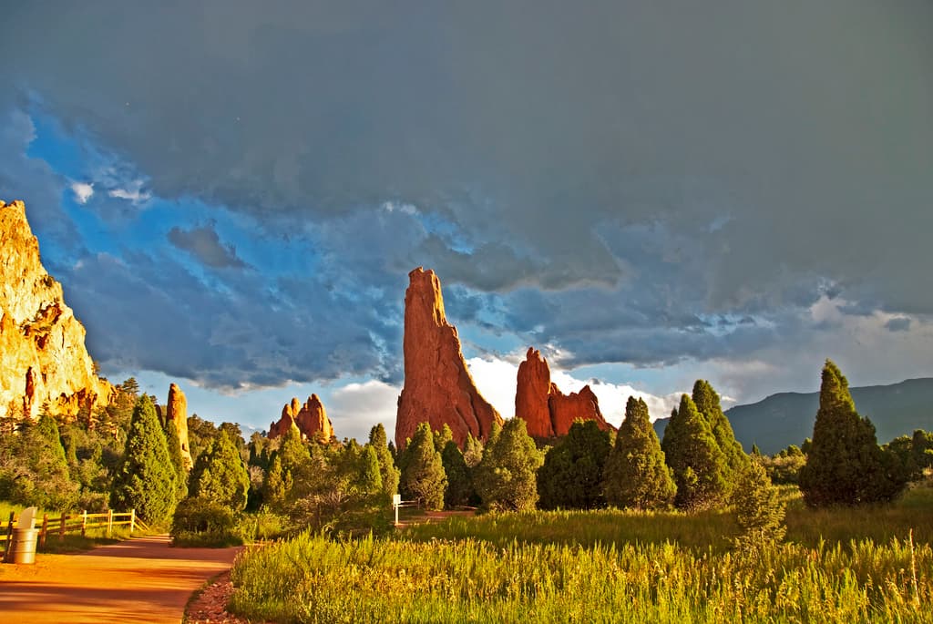 Rugged slabs of red rock jut up from the ground like sharp teeth at the Garden of the Gods near Colorado Springs. The tall rock slabs are surrounded by small evergreen trees.