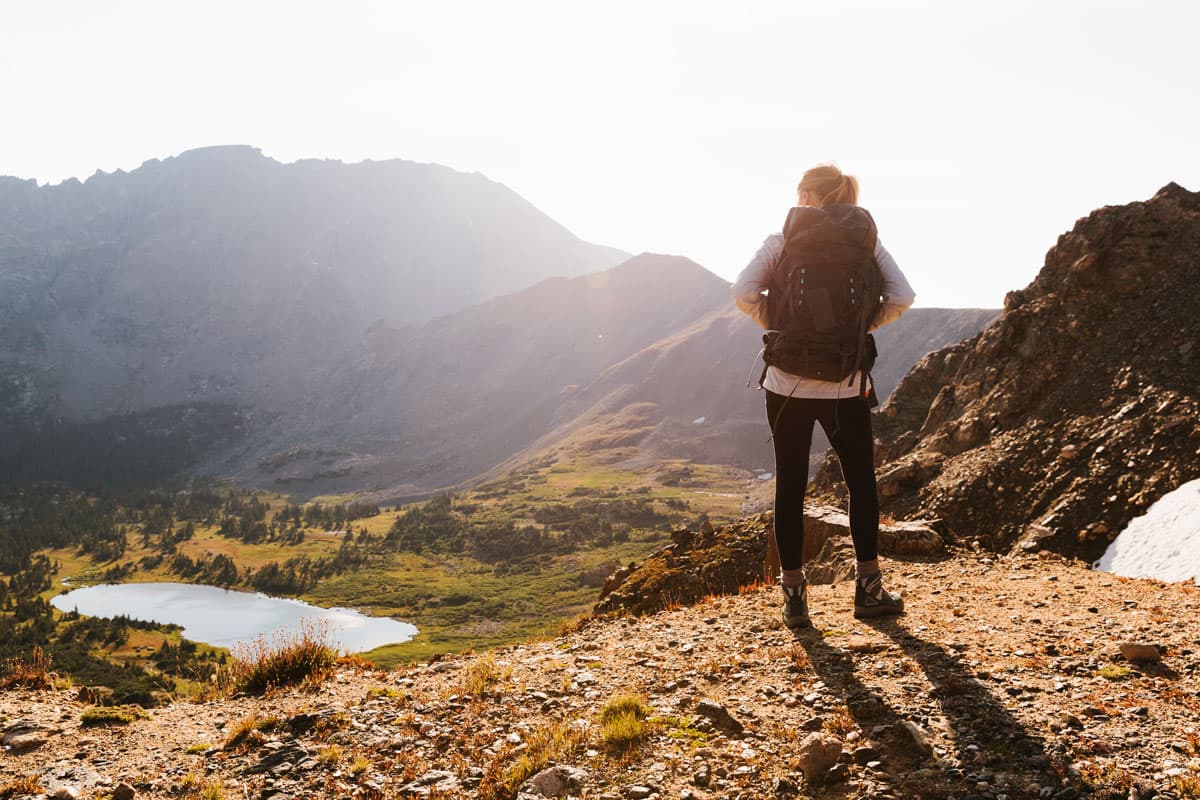 A hiker stands on an overlook as the sun shines over the mountains