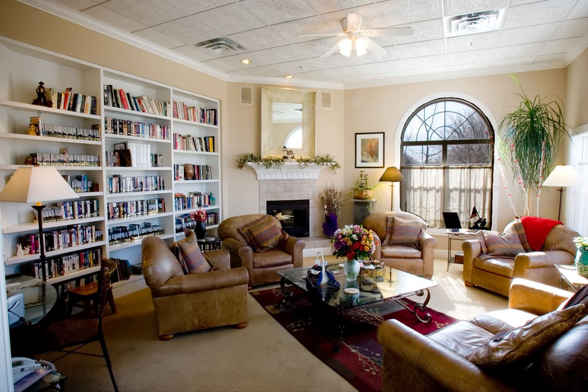 A large living room in Colorado Springs is set up with white built-in shelves that are filled with books and movies and five, thickly padded leather chairs.