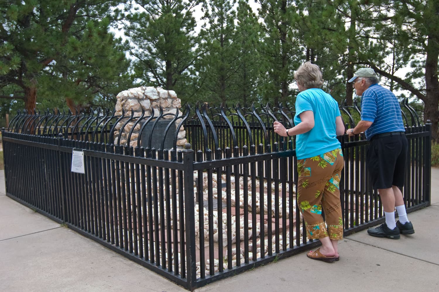 Two people lean against the black, iron fence and look at the gravesite of the famous Buffalo Bill on Lookout Mountain in Golden, Colorado.