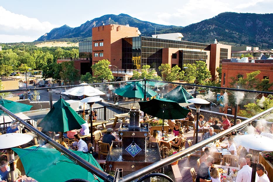 The view of the Flatirons from the Rio Grande Restaurant's rooftop patio in Boulder where people are eating on a sunny day