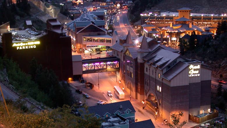 Bustling downtown Black Hawk at night. Cars and buses make their way under big buildings with sky bridges going across the streets.