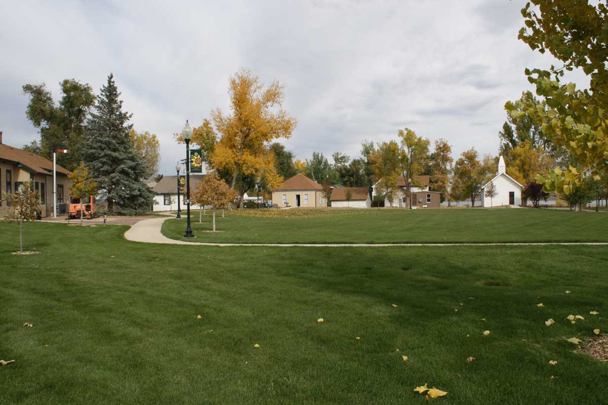 Windsor's Boardwalk Park Museum ha.s a green lawn with small buildings in the background under a white clouded sky.