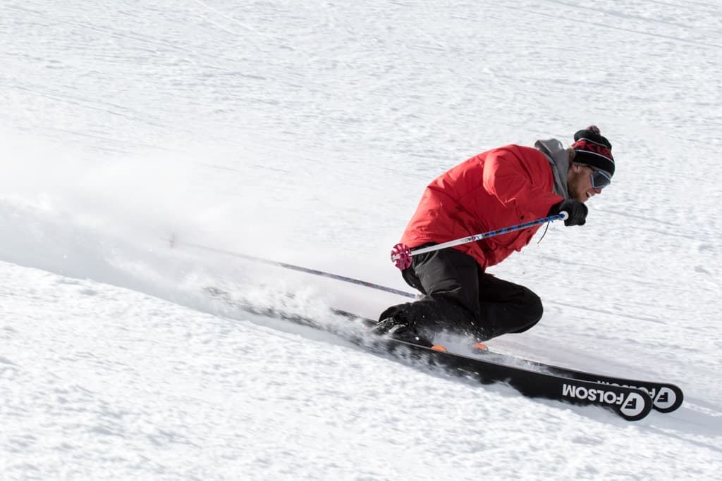 A ski in a red jacket and ski hat makes a carving turn with their Folsom Custom Skis on a bumpy mountain slope in Colorado.