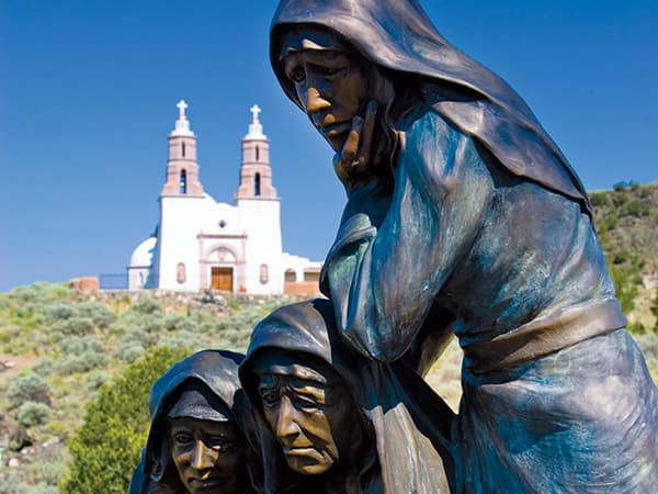 A metal statue sits in the foreground with a large white church behind it