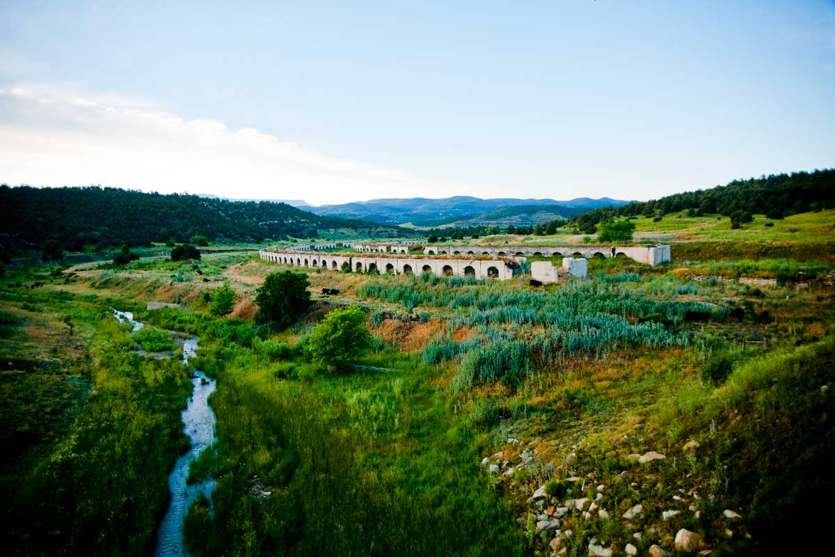 A verdant field of green grasses and trees sits in the foreground with the Historic Coke Ovens in the distance.