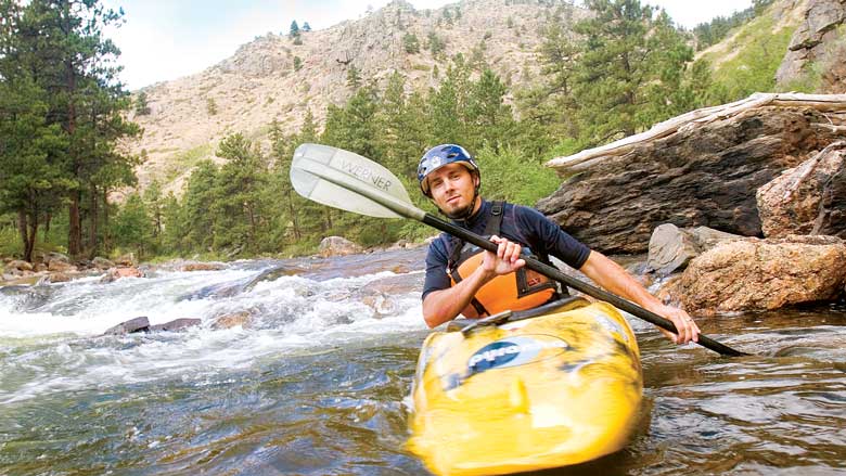A person sits in a banana-yellow kayak and paddles along the rushing waters of the Cache La Poudre River in Colorado.