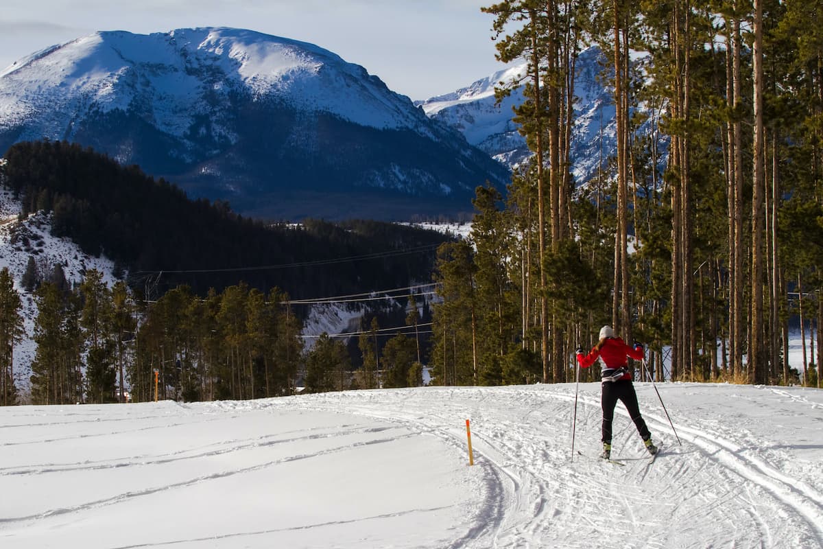 In a vast, flat, snowy meadow, a cross-country skier in a red jacket pushes foward using their poles