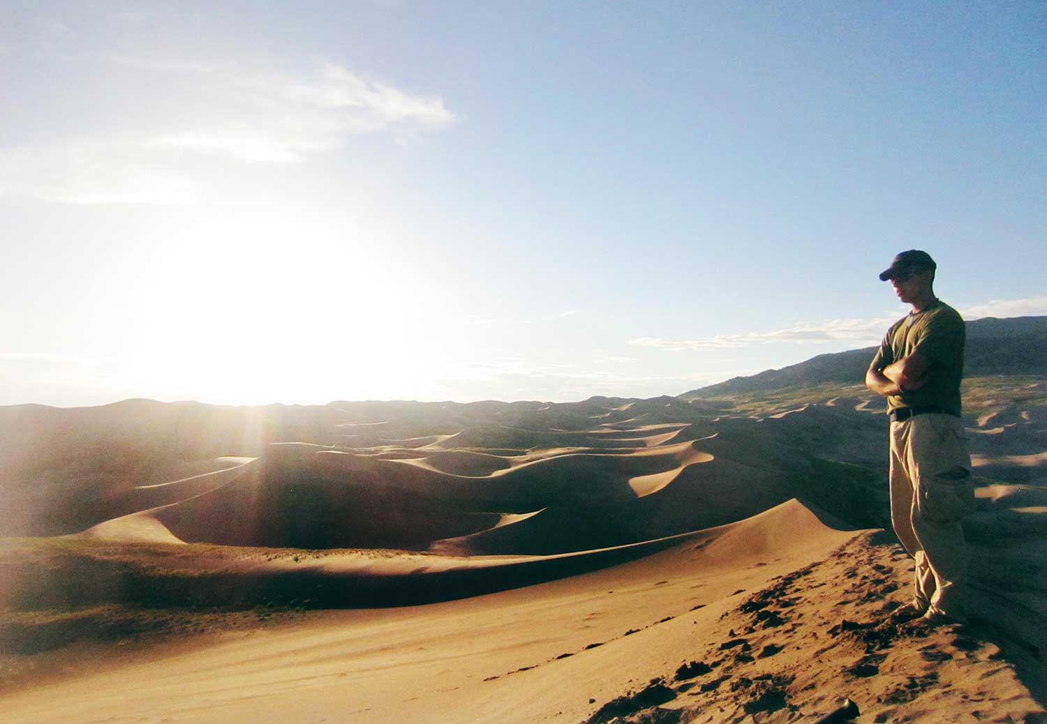 A man stands at an overlook watching a sunset over sand dunes