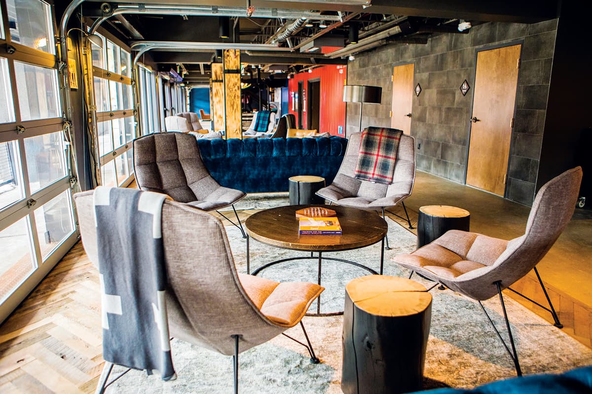 Four cozy, gray fabric lounging chairs without arm rests are arranged around a wooden coffee table at Gravity Haus in Breckenridge, Colorado.