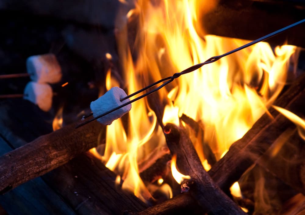 A marshmallow on a stick roasts over a fire
