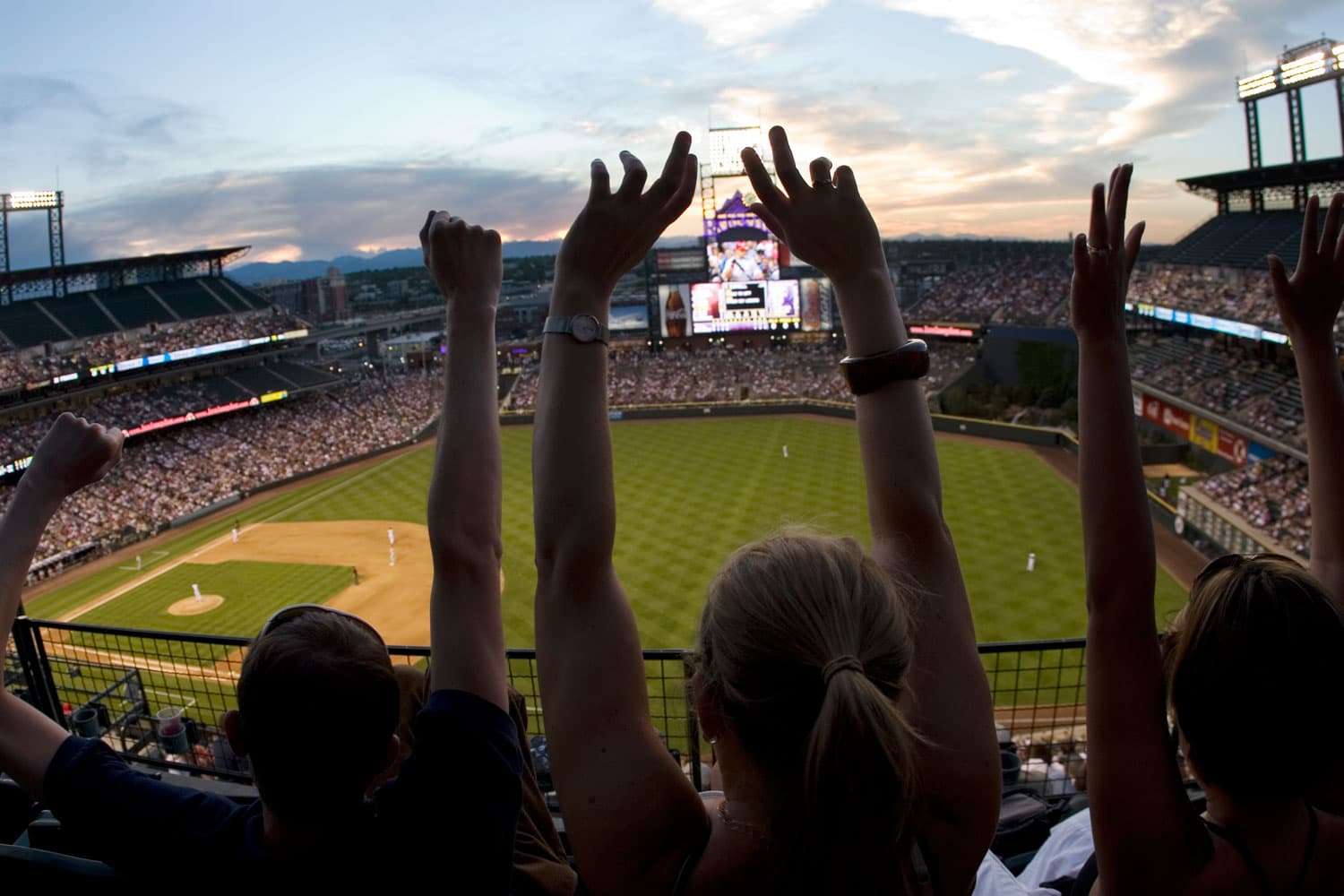 Up in the nosebleed seats, a group of fans throw their hands up in celebration as they look down on the baseball field below