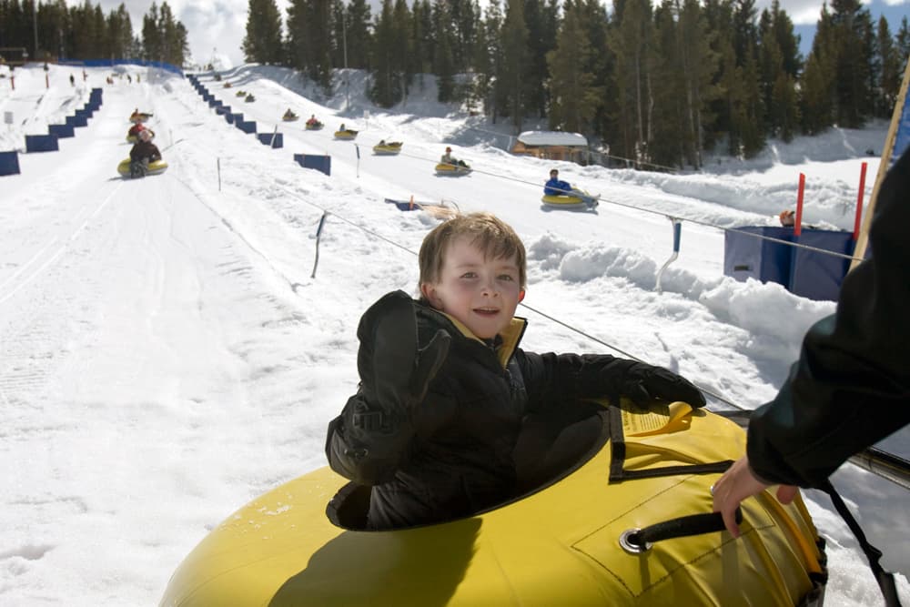 A boy in a yellow intertube waits his turn to be pushed down a gently sloped snowtubing course
