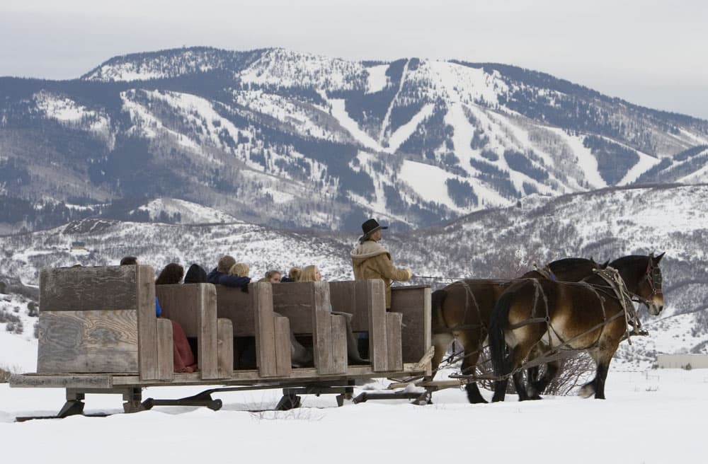 A team of two horses pulls a simple wooden sleigh with multiple rows of passengers near the ski slopes of Steamboat Springs, Colorado.