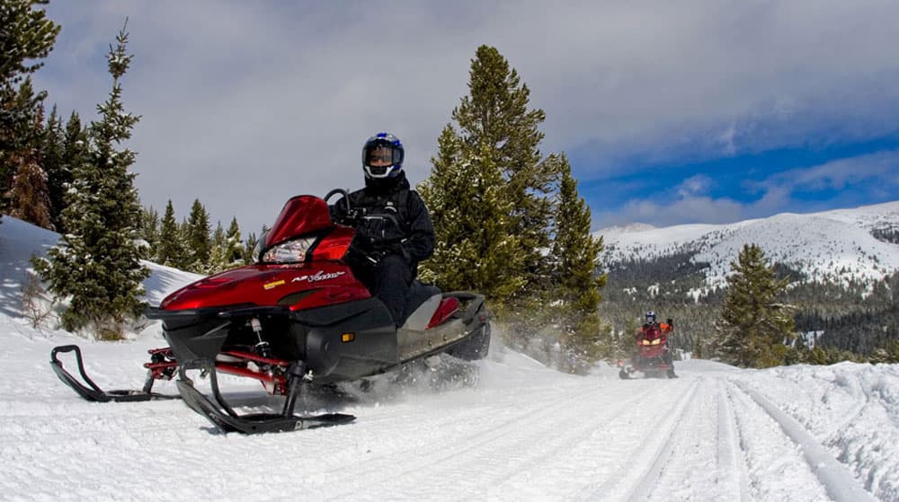 A person in a red snowmobile steers his sled along a snowy trail