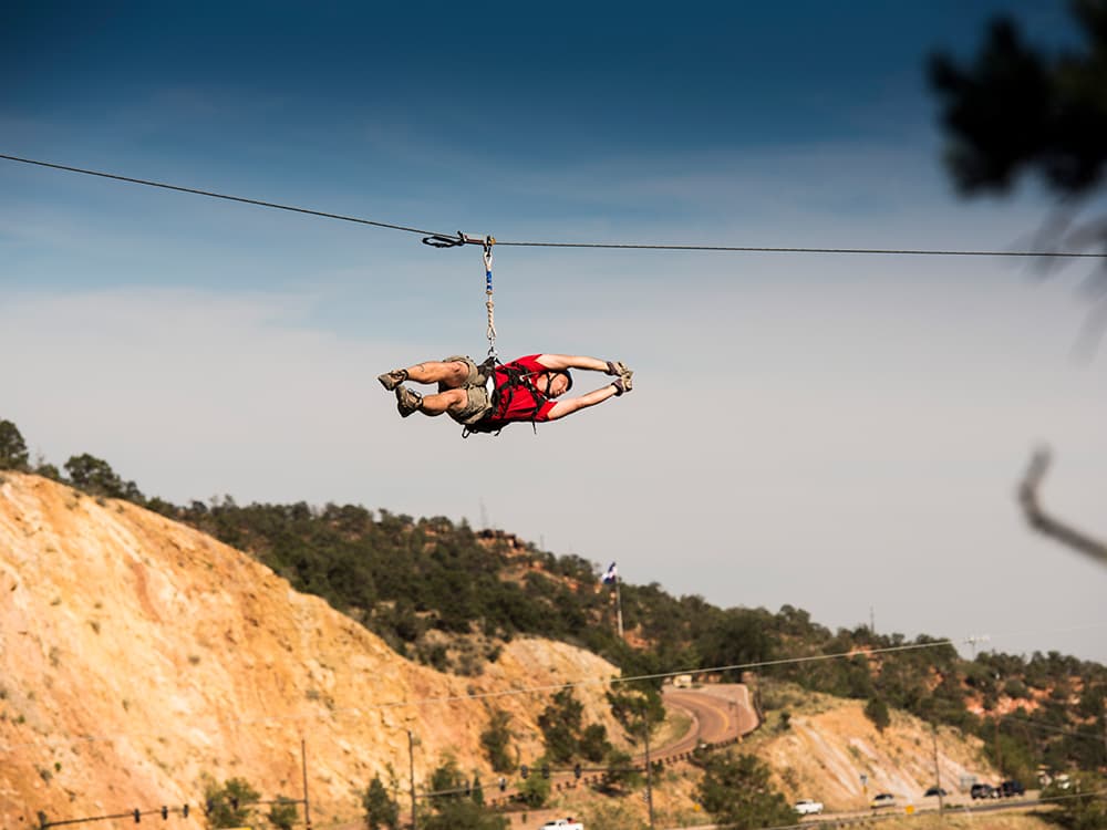A zipliner in red shirt stretches out as they zoom through the air on a thrilling ride in Manitou Springs, Colorado.