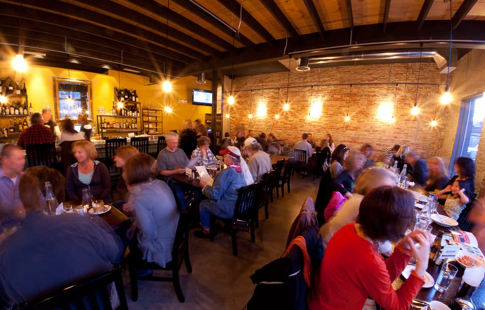Diners sit at tables in a dining room. Above them, sparkly lights give the room a warm glow.