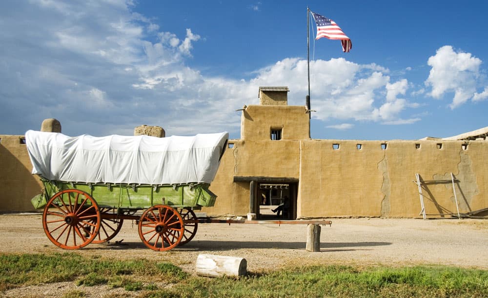 An old fashioned chuckwagon is stopped in front of a large, sand colored building at Bent's Old Fort National Historic Site near La Junta, CO
