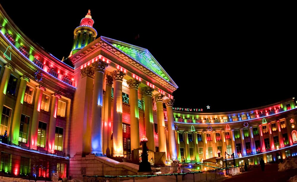 A city building in Denver, Colorado, is lit up with vibrant red, green, orange and blue holiday lights, along with lit images of bells and stars.