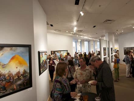 A group of patrons gathers around a few paintings in a white-walled gallery