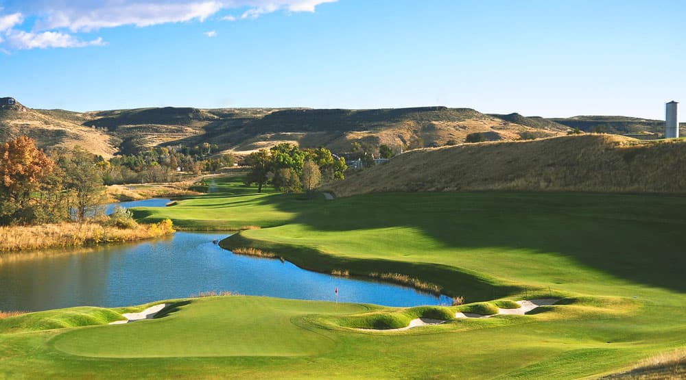Rugged, brown plateaus surround a verdant golf course complete with sand traps, undulating hills and a small lake near Golden, Colorado.