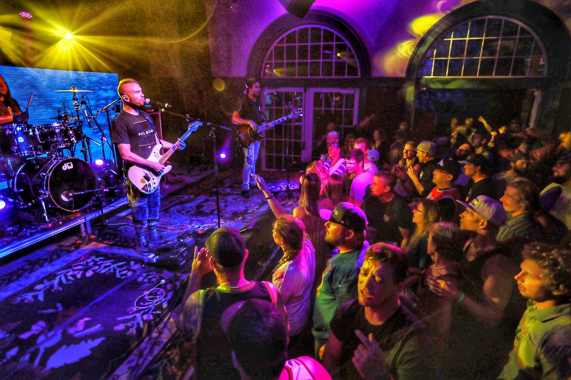 Colorful lights glow on the walls and crowd at an intimate concert at the Ivy Ballroom