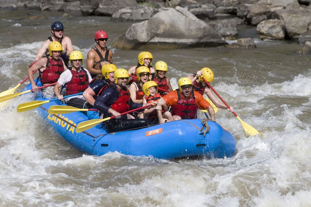 A group of people in a raft splash through whitewater rapids surrounded by rocks