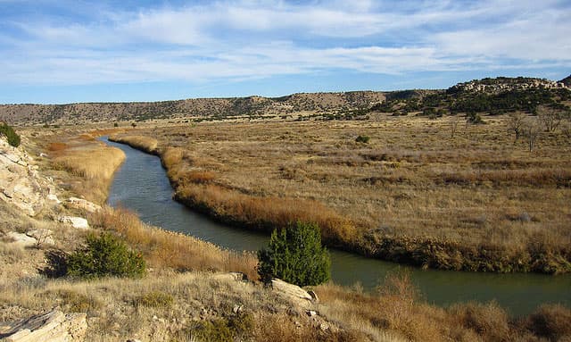 Near La Junta, Colorado, a small river winds its way around mountains and yellow prairie lands dotted with sparse trees and evergreen shrubs.