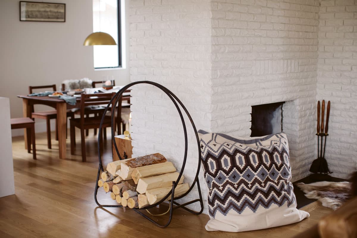 Logs sit in a holder in a cozy room with white brick walls and patterned pillows