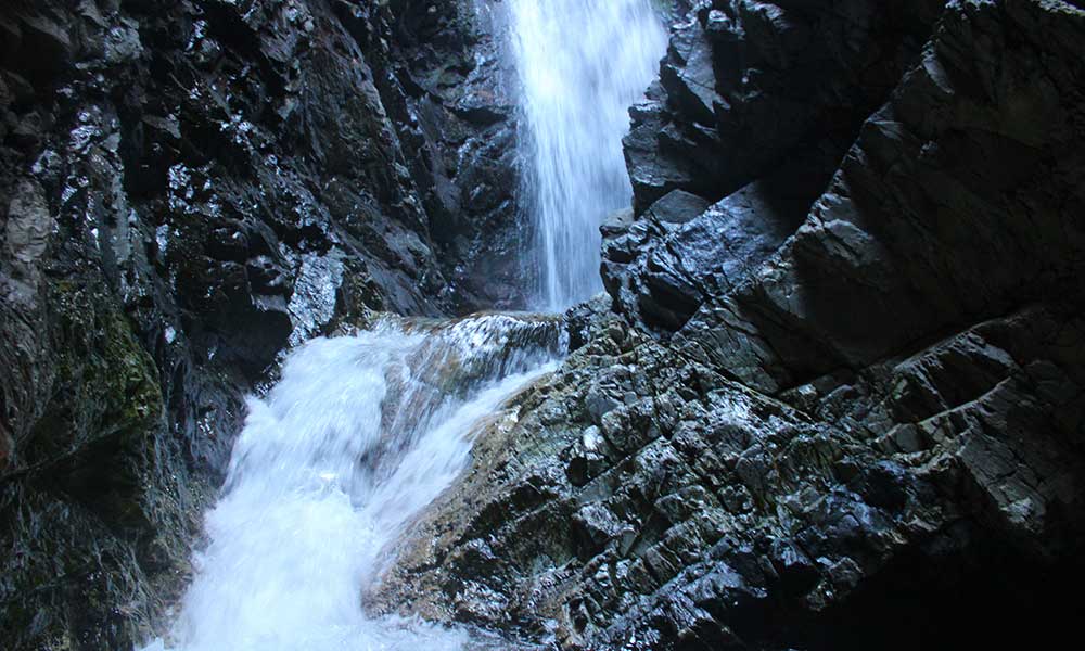 A rushing waterfall through sharp and jagged black rocks at Zapata Falls.