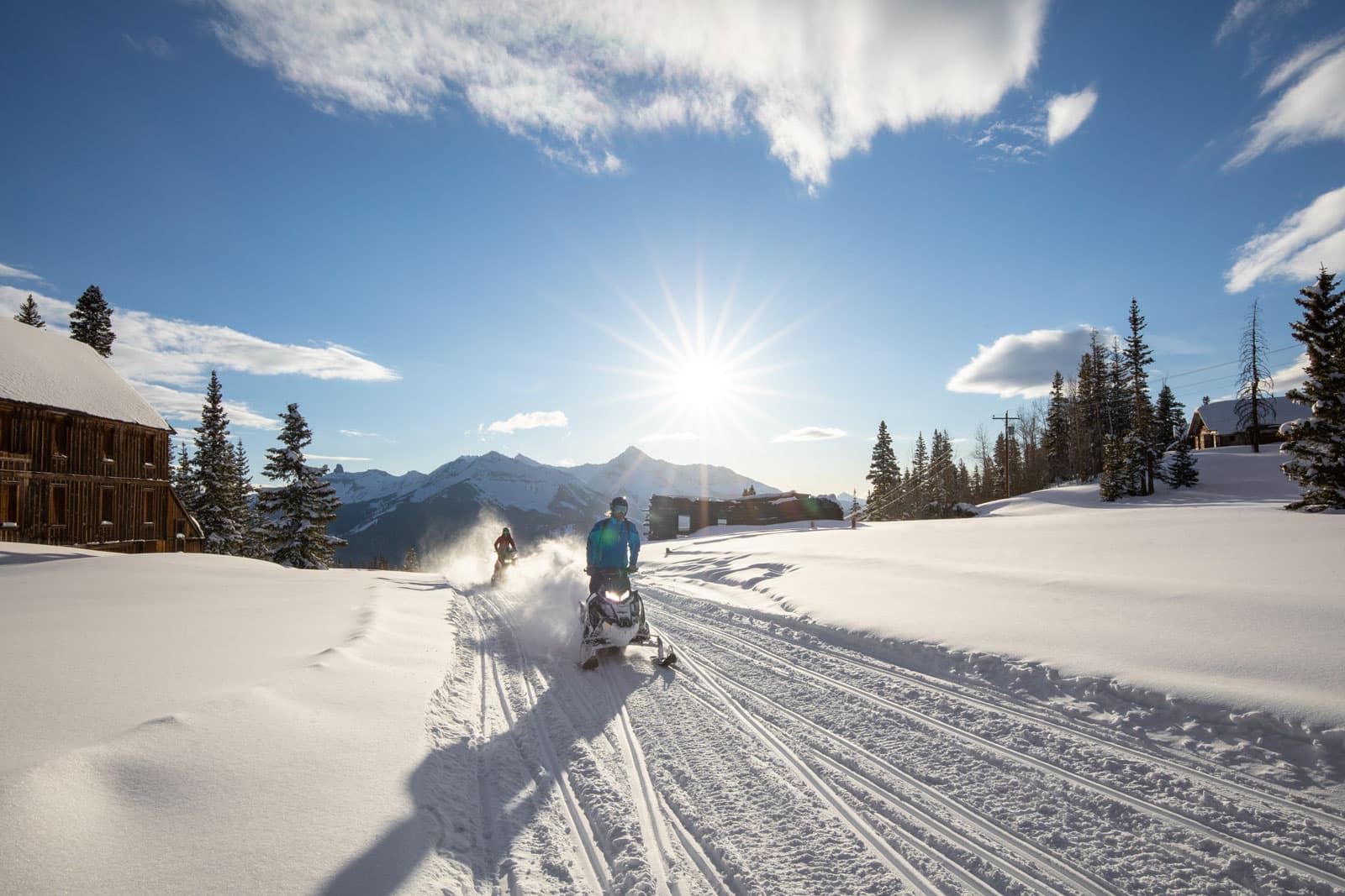 Snowmobilers make tracks underneath a sunny blue sky