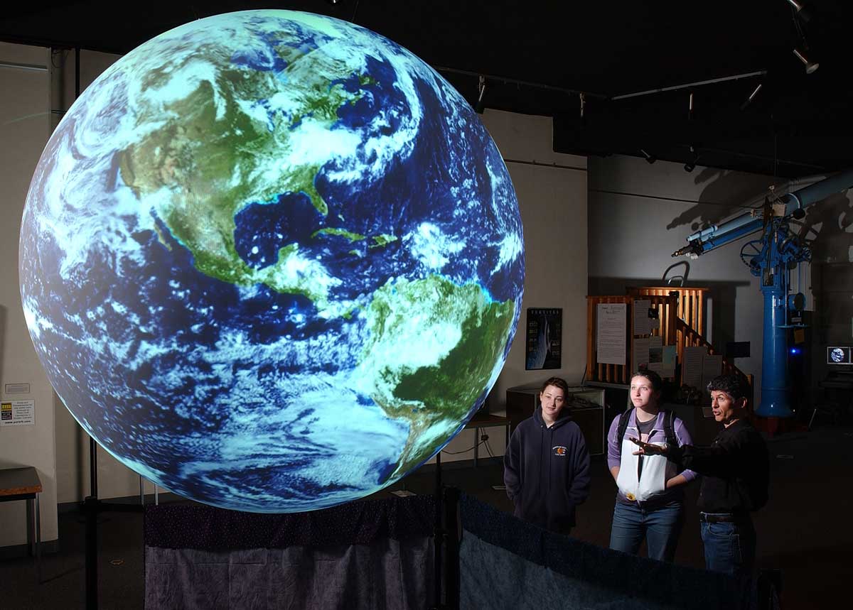 Three people gaze at a giant illuminated globe